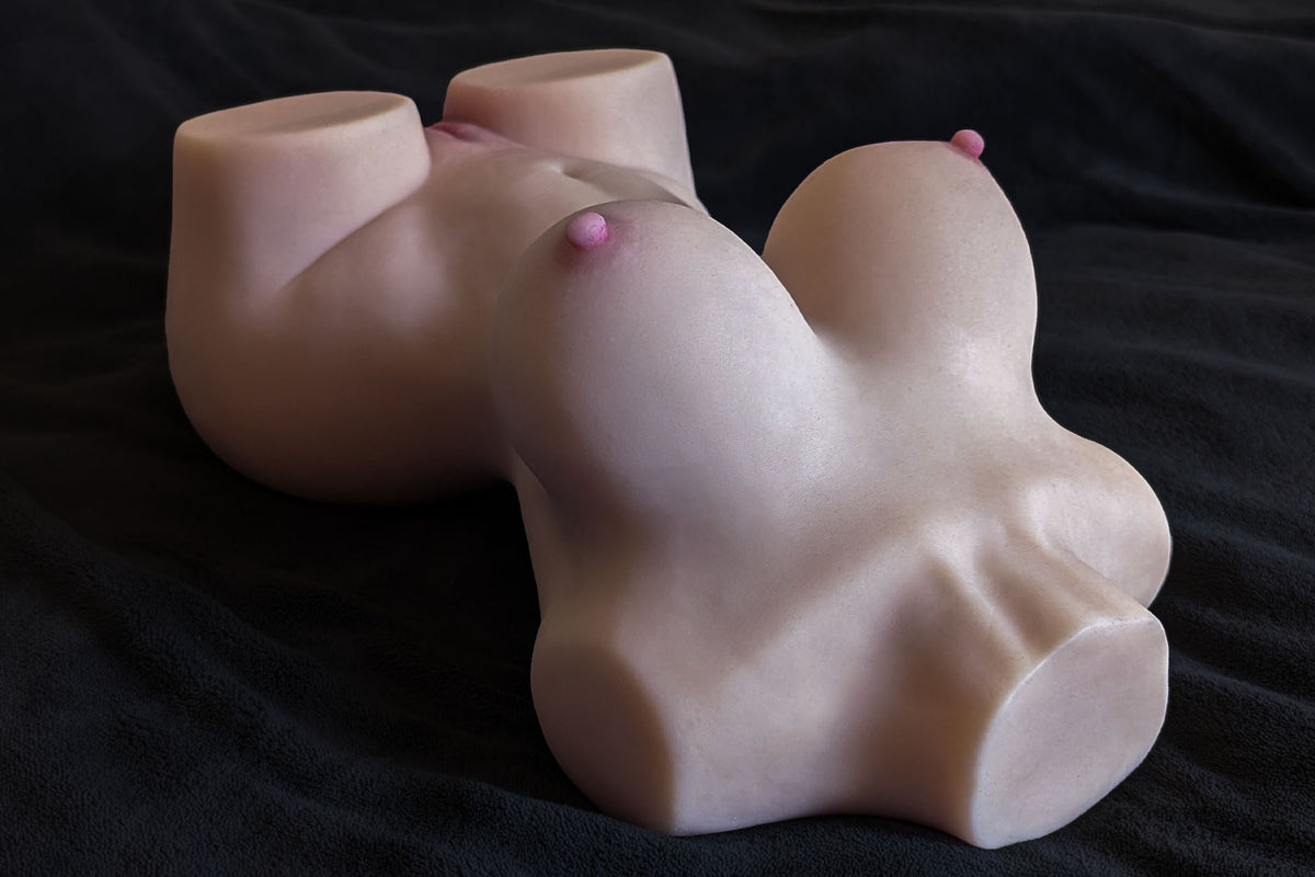 Sex doll torso Sara distesa su una superficie scura, vista laterale con seno